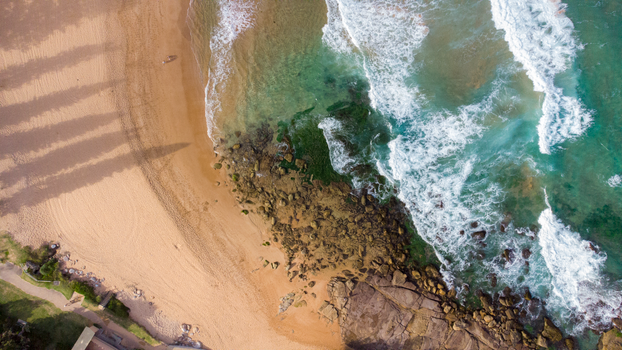 Stunning aerial shot of a sandy beach, rocks, and turquoise waves crashing on the shore.