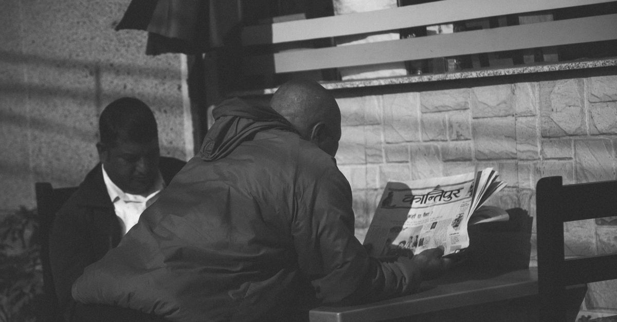 A traveler sitting at a small outdoor café, reading a local newspaper, surrounded by locals in an un-touristy neighborhood