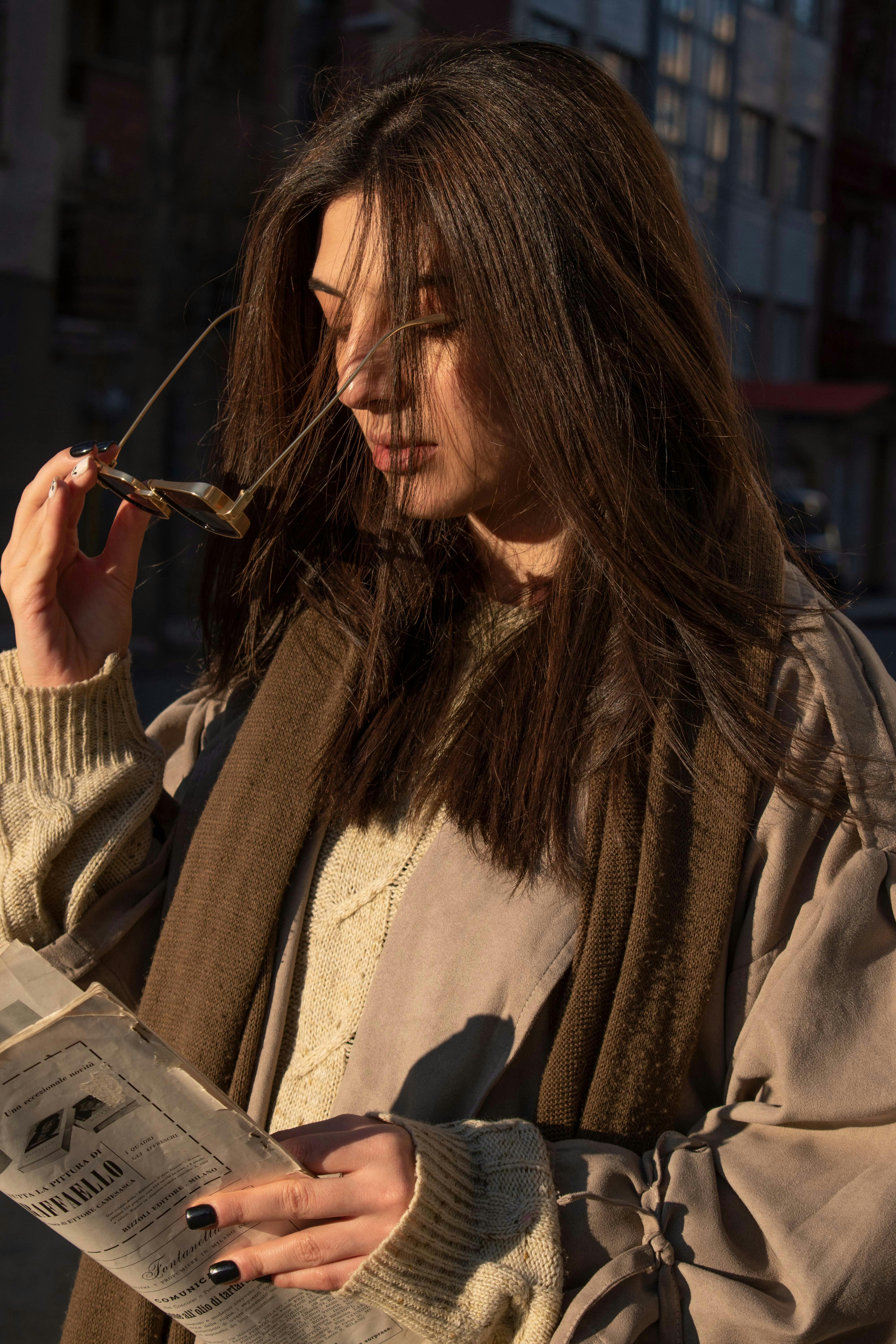 a woman reading a newspaper while standing on a street