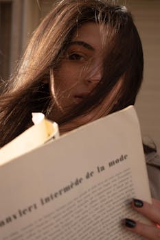 Woman outdoors reading a fashion magazine, her hair blowing in the wind, creating an intimate and thoughtful mood.