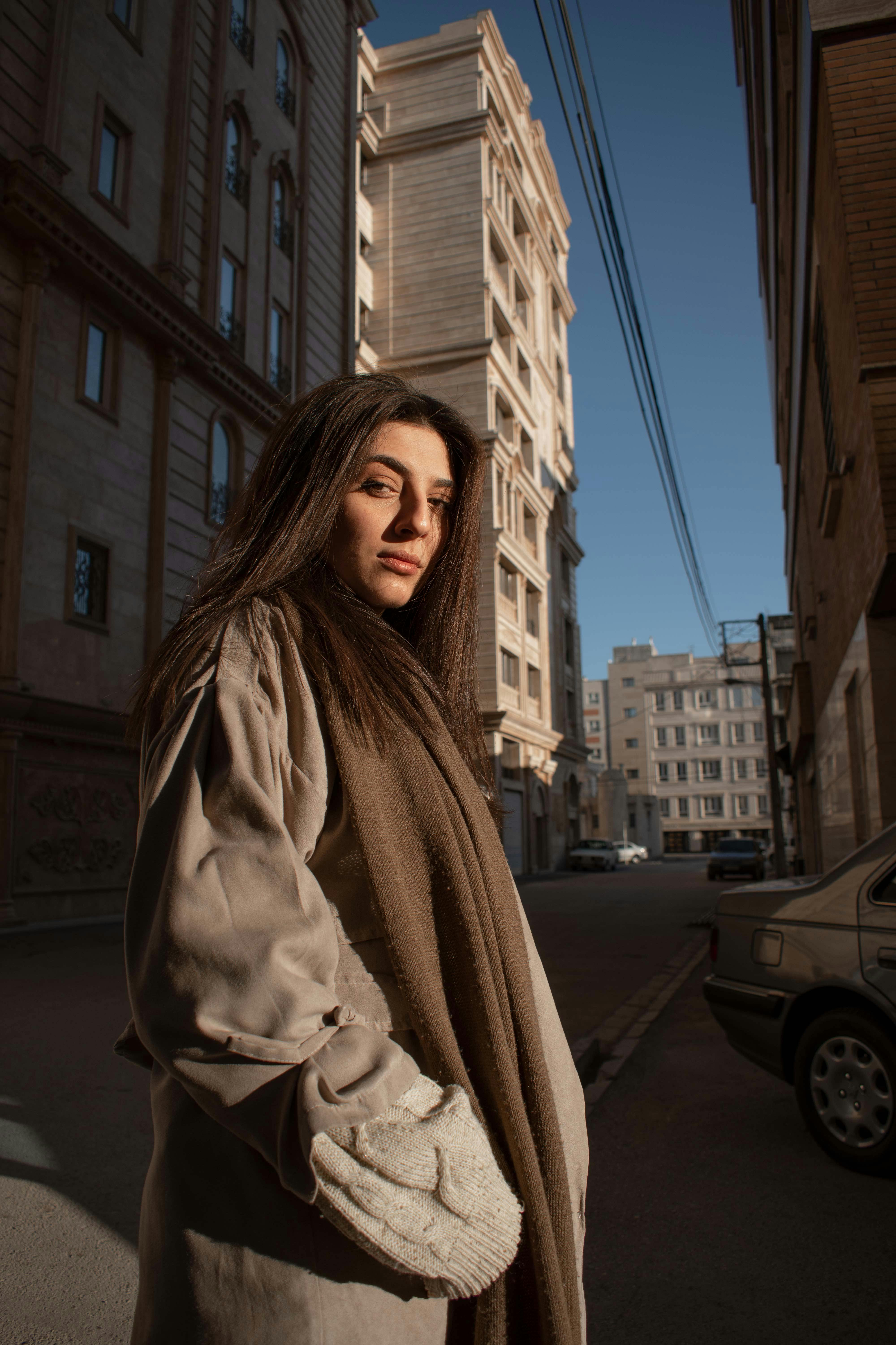 a woman in a long coat standing in the middle of a city street