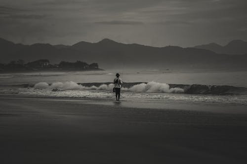 A Grayscale Photo of a Fisherman Standing on the Beach