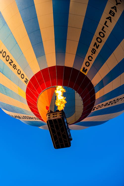 Free Low angle view of a colorful hot air balloon with a visible flame against a blue sky. Stock Photo