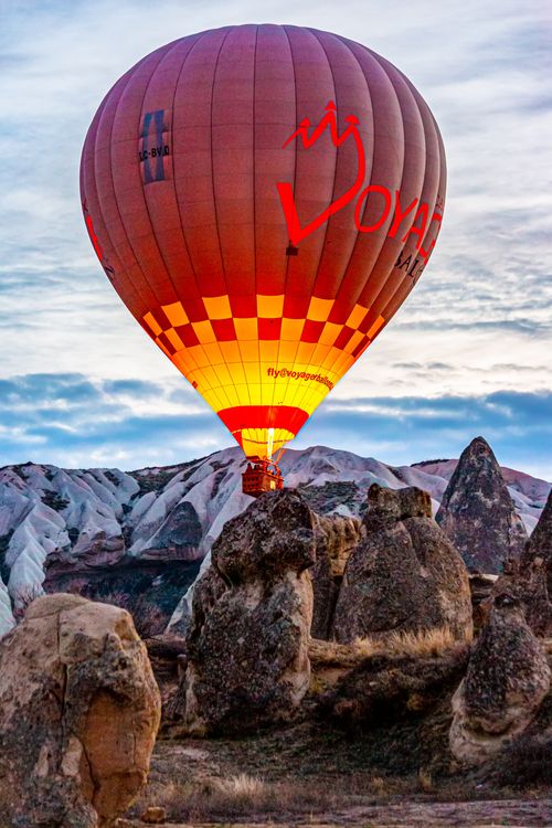 Free A vibrant hot air balloon floats over Cappadocia's unique rock formations at sunrise, showcasing stunning natural beauty. Stock Photo