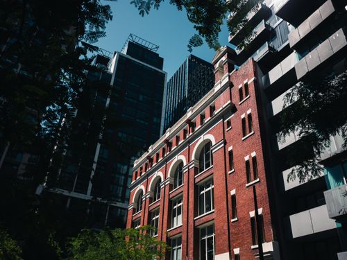 Free Dramatic low-angle shot of sunlit urban buildings, highlighting red brick and contrasting modern glass towers. Stock Photo