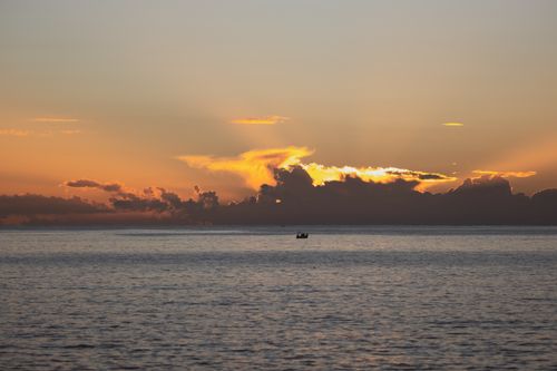 Free A peaceful boat silhouettes against a vibrant ocean sunset with dramatic clouds. Stock Photo