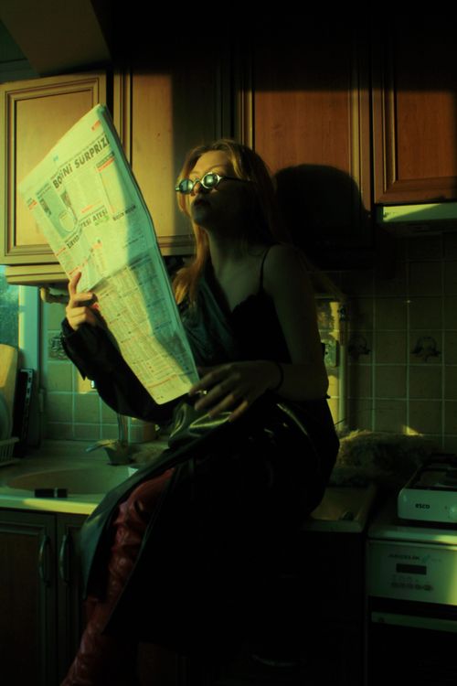 Free A woman sits in a sunlit kitchen reading a newspaper, wearing sunglasses. Stock Photo