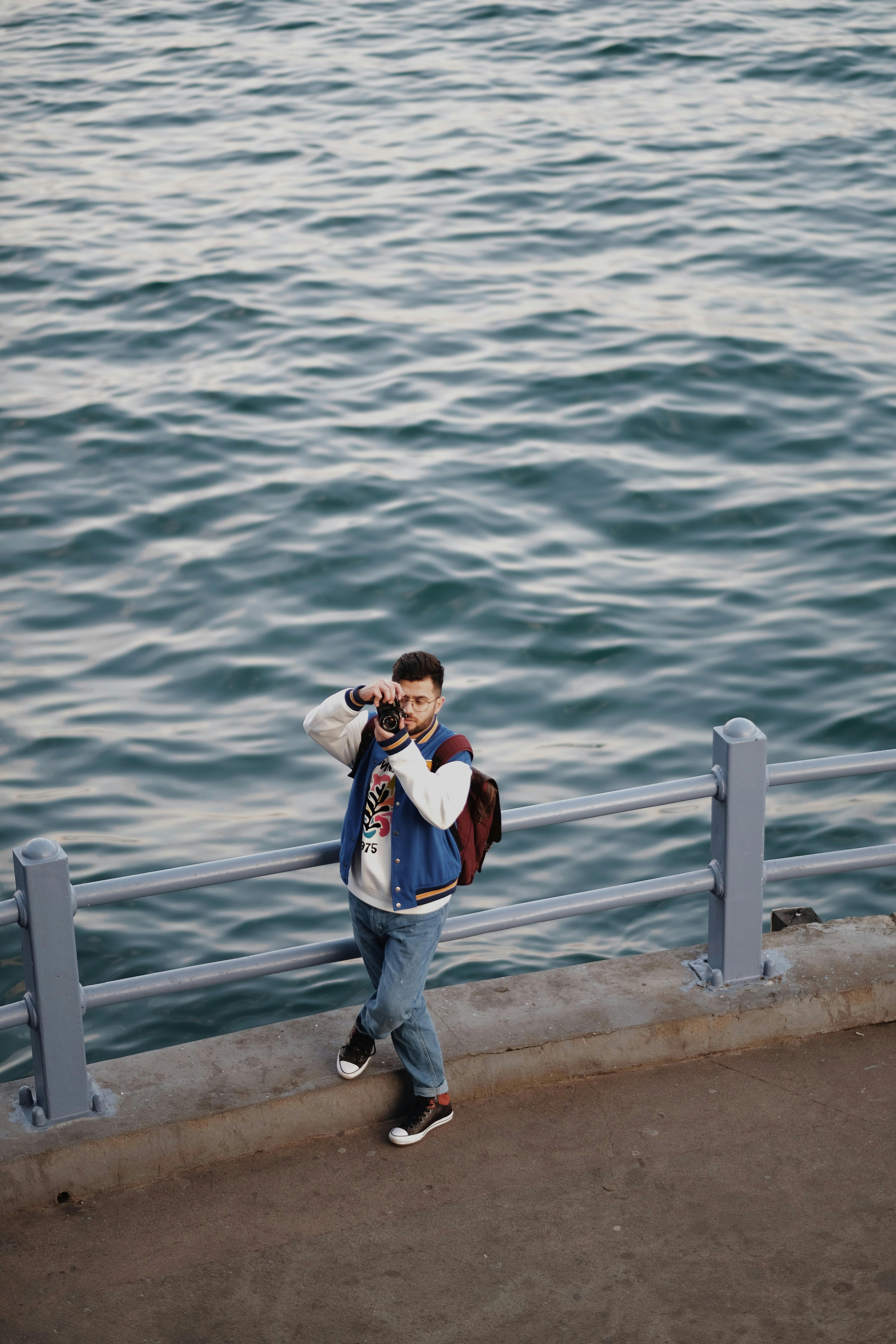 Free A man takes pictures by the shore, standing confidently with the camera. Stock Photo