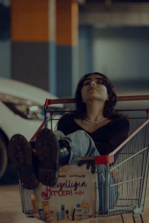 Free A young woman sits with closed eyes in a shopping cart in an indoor parking garage, showcasing a moment of rest. Stock Photo