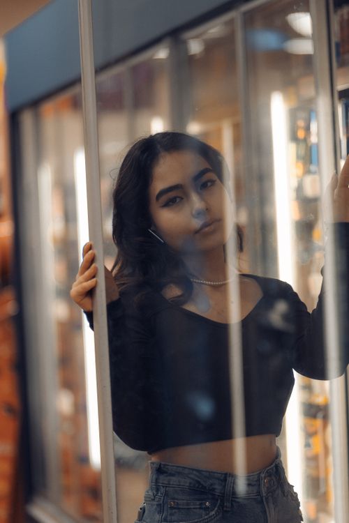 Free Young woman with long hair posing behind glass indoors, showcasing a fashionable look. Stock Photo