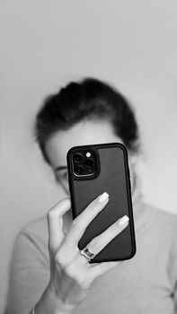 Monochrome image of a woman capturing a selfie using her smartphone indoors.