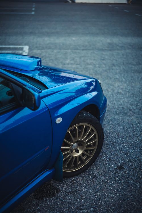 Free High angle view of a stylish blue sports car with gold alloy wheels on a wet asphalt surface. Stock Photo