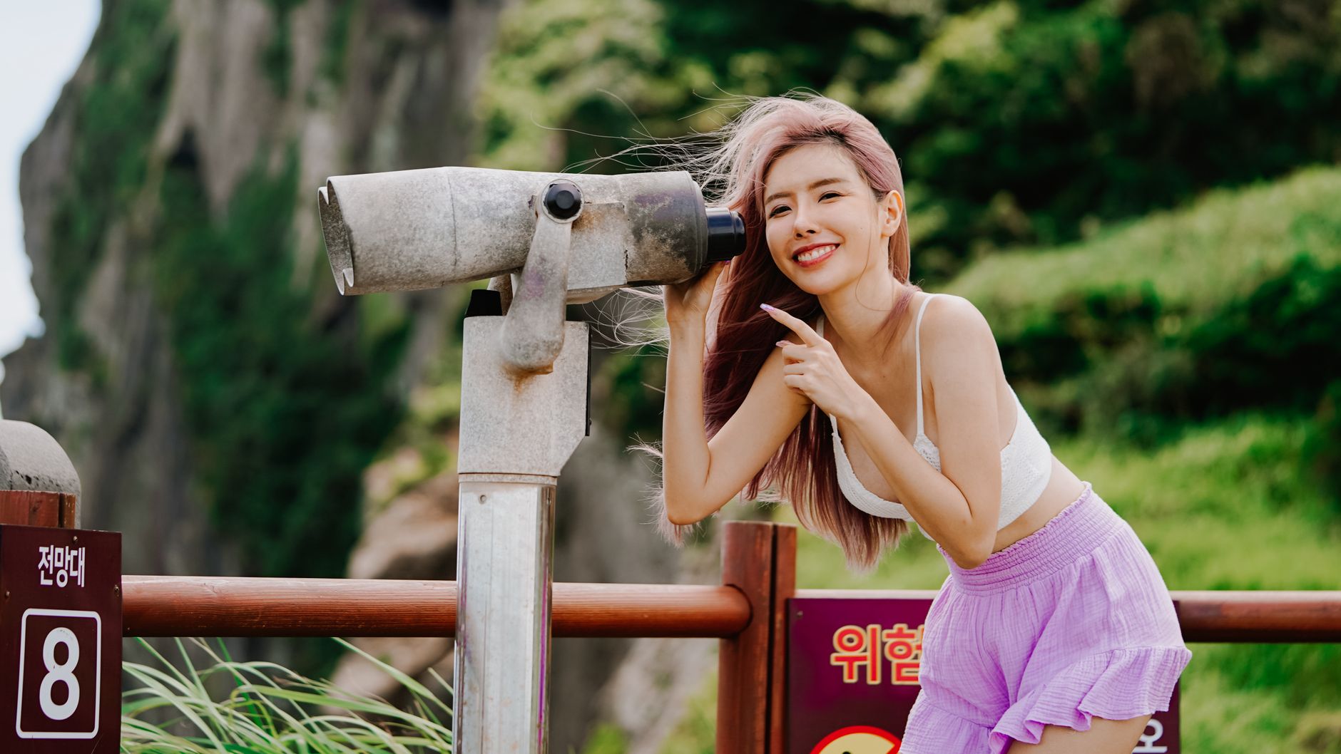 Woman with pink hair enjoying a scenic view through binoculars on a sunny day.