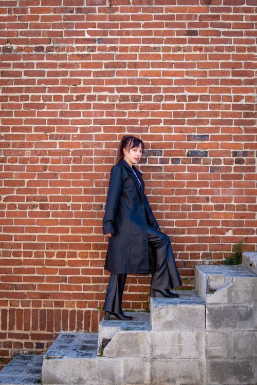 Free Fashionable woman posing on steps against a classic brick wall, showcasing urban style. Stock Photo
