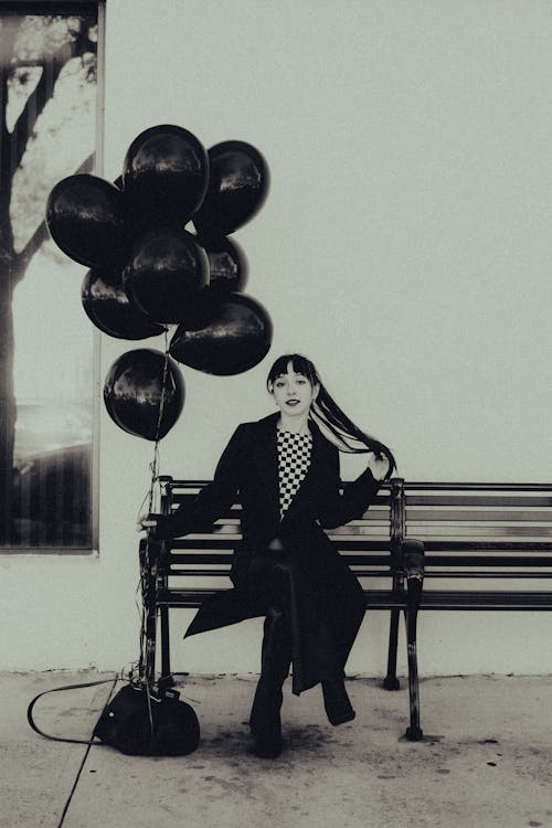 Black and White Photo of Woman Sitting on a Bench Holding Balloons 