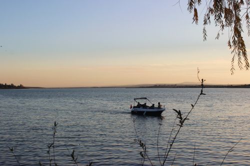 Free Motorboat on a serene lake at sunset with scenic views and silhouette of people. Stock Photo