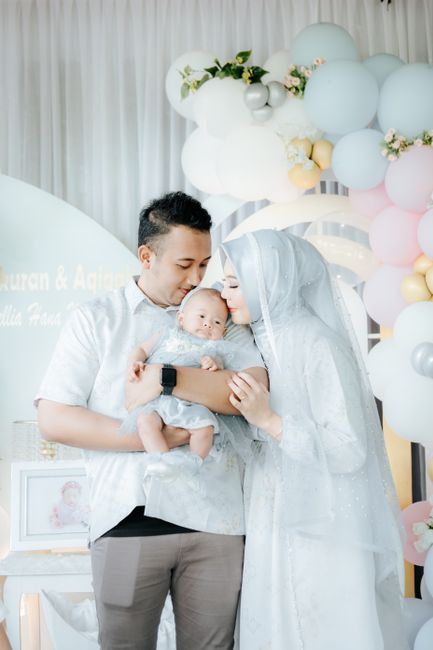 Loving parents holding their newborn baby at a celebratory gathering with festive decorations.