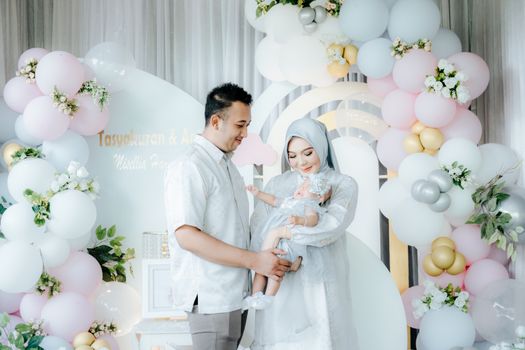 A family celebrating with pastel balloons, parents in elegant attire holding their baby. - Fotografer Sidoarjo