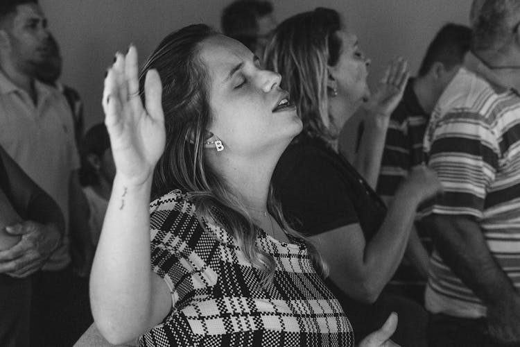 Woman Singing With Raised Hand And Closed Eyes At Congregation