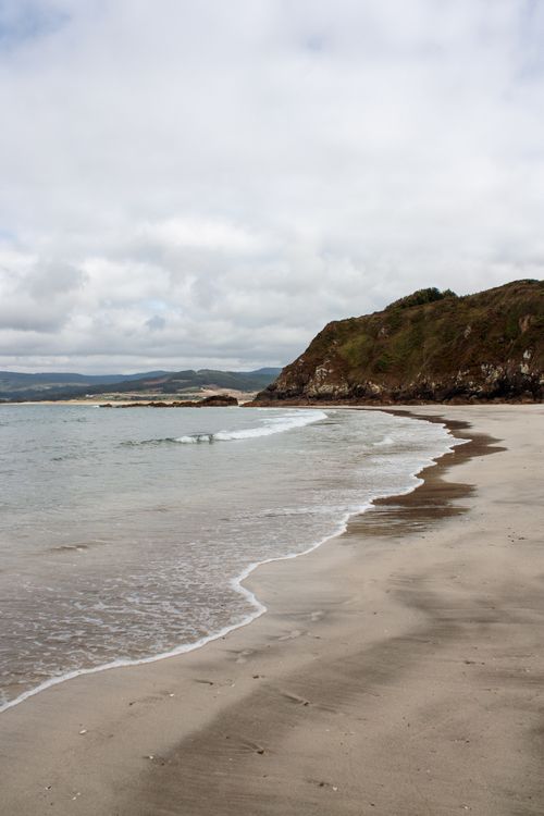 Free Peaceful beach view with waves lapping on a sandy shore under cloudy skies. Stock Photo