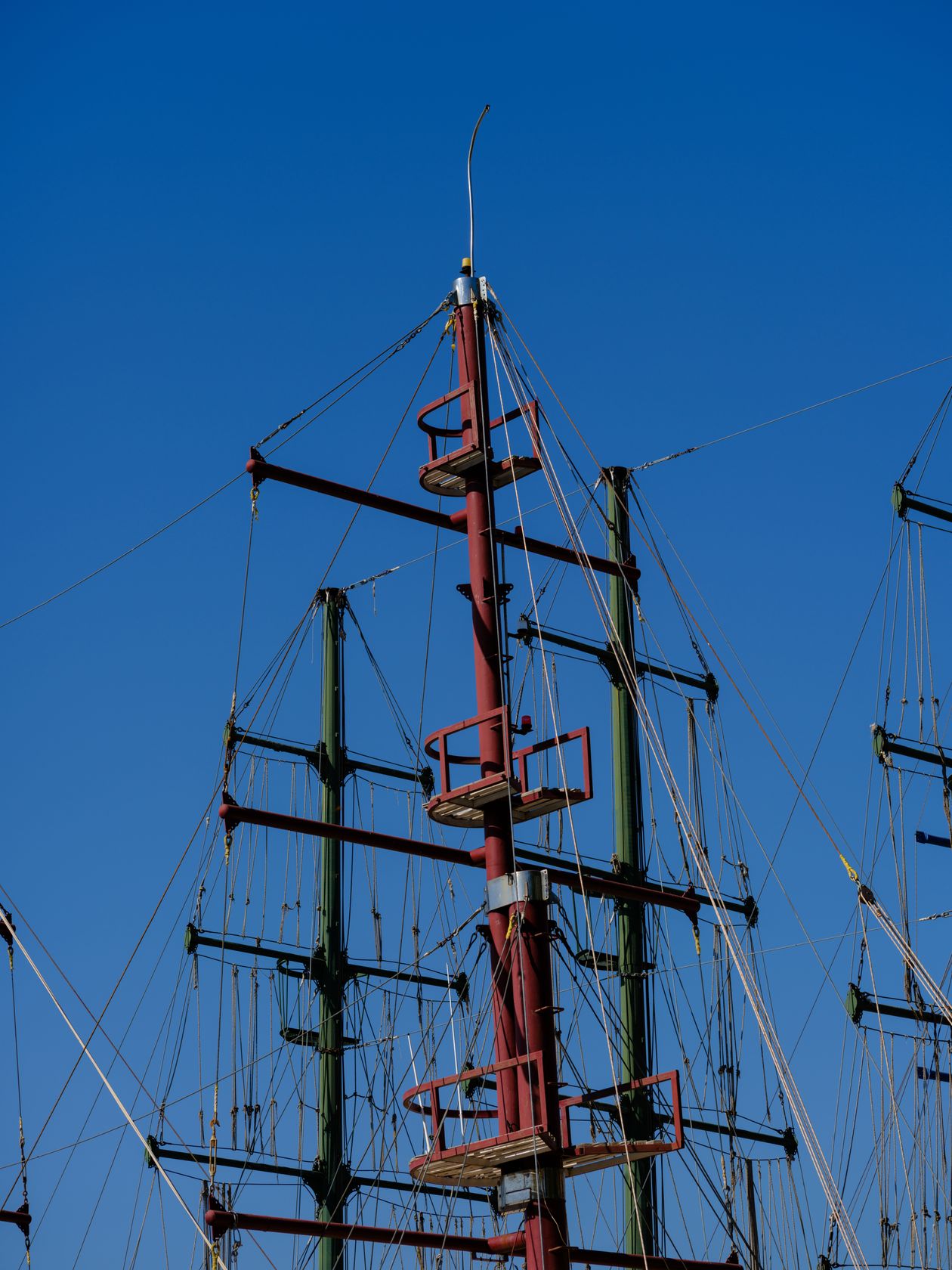Close view of tall ship masts and rigging rising against a bright blue sky over an old sailing vessel