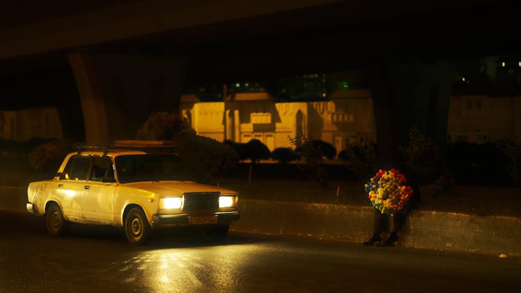 Car Near Person Sitting With Balloons By Street At Night