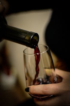 A close-up view of red wine being poured into a glass by a woman's hand.
