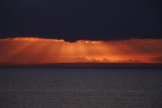 Vibrant sunset over the sea with dramatic clouds and sun rays creating a scenic view.