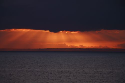 Free Vibrant sunset over the sea with dramatic clouds and sun rays creating a scenic view. Stock Photo