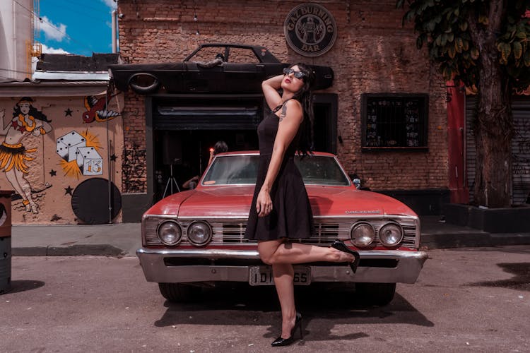 Woman In A Black Dress Posing In Front Of A Red Car