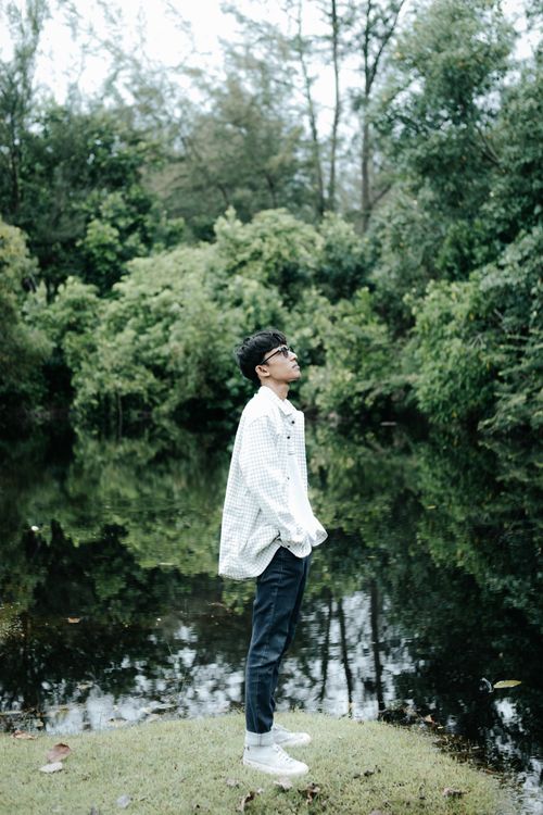 Free Man standing in a serene park by a tranquil pond, immersed in nature. Stock Photo