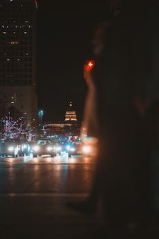 Nighttime city scene with traffic and blurred pedestrians on a street illuminated by lights.