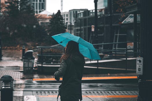 A woman with a blue umbrella walks through a city street on a rainy day, capturing the essence of urban life.