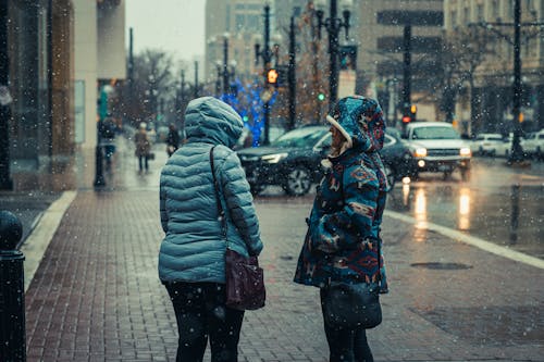 Women Talking on Sidewalk in City under Snowfall