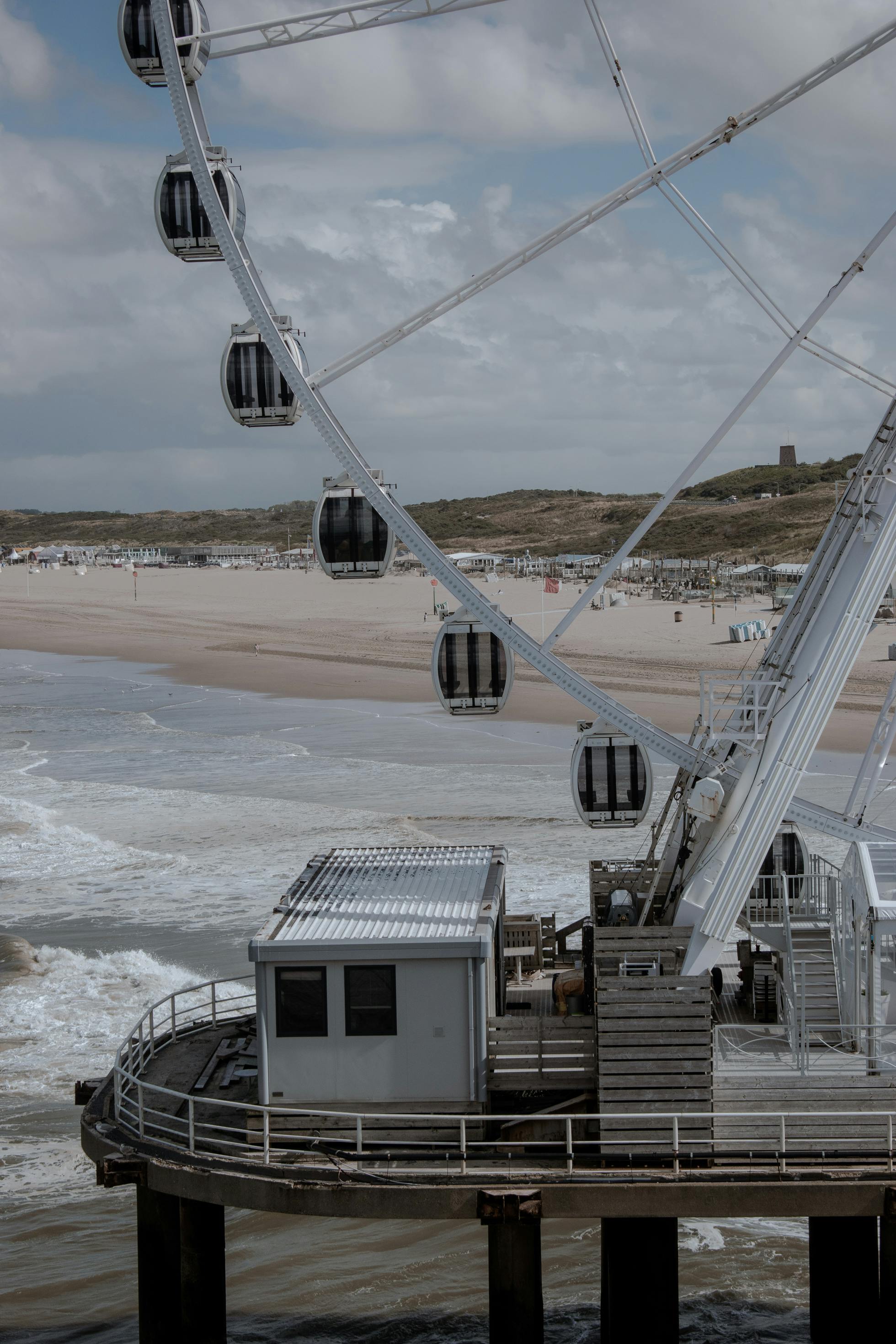 Aerial view of a Ferris wheel on a pier overlooking a sandy beach and ocean waves in The Hague.