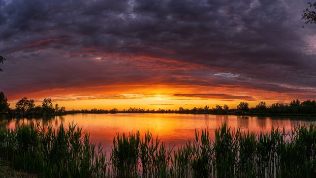 Breathtaking sunset over a tranquil lake with dramatic clouds and serene reflections.