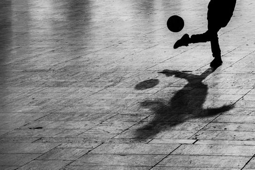 Shadow of a person kicking a football on a paved outdoor surface.
