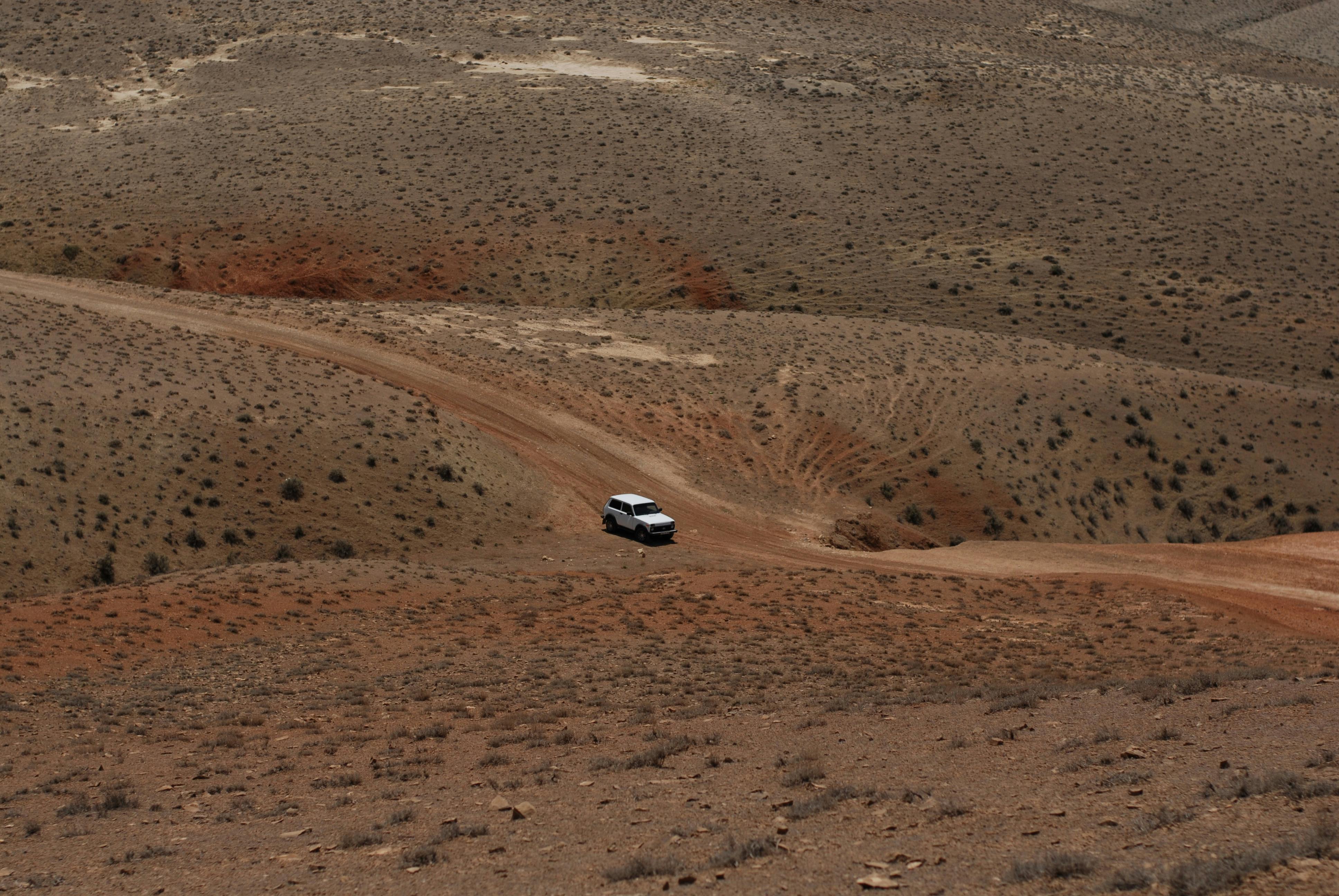 A solitary off-road vehicle traverses a rugged desert dirt road under a clear sky.