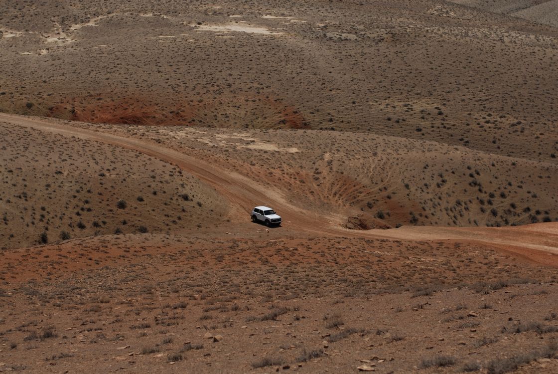 Vehicle driving a dirt road across a wide desert valley