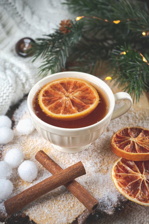 A Cup of Tea with a Slice of Orange and Cinnamon Sticks and Christmas Decorations Lying Around 