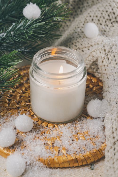 Free A lit candle in a glass jar surrounded by holiday decorations and faux snow creating a warm winter ambiance. Stock Photo