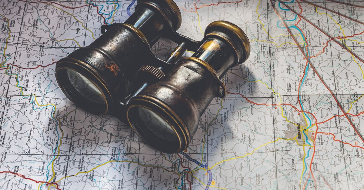 Binoculars resting on a folded map representing site-wide keyword search across competitor websites