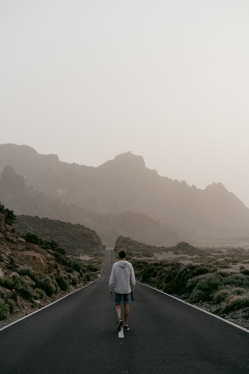 Free A solitary traveler walks down a mountain road, capturing serenity and exploration. Stock Photo