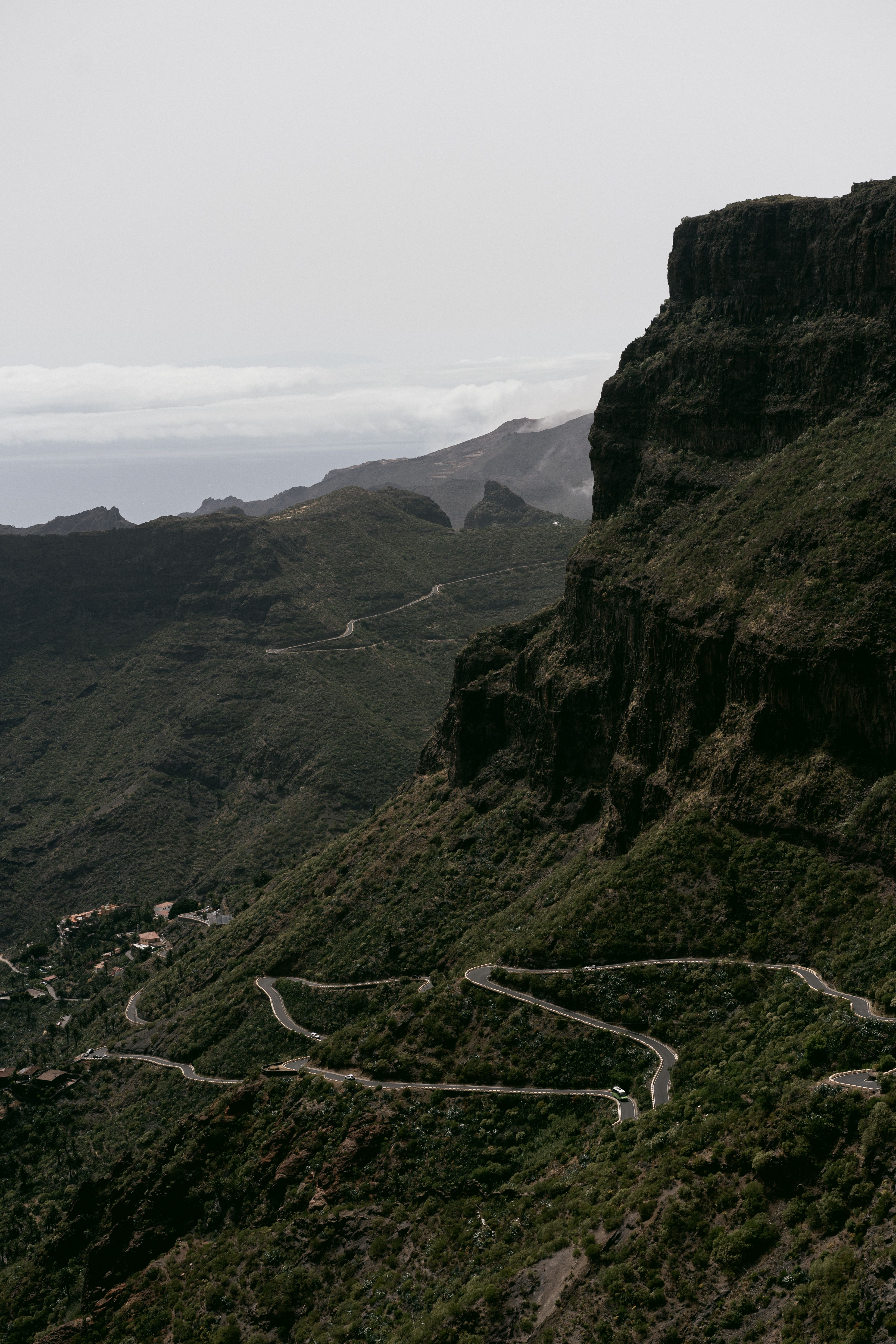 Aerial view of a winding road through a lush mountain range, under a cloudy sky.