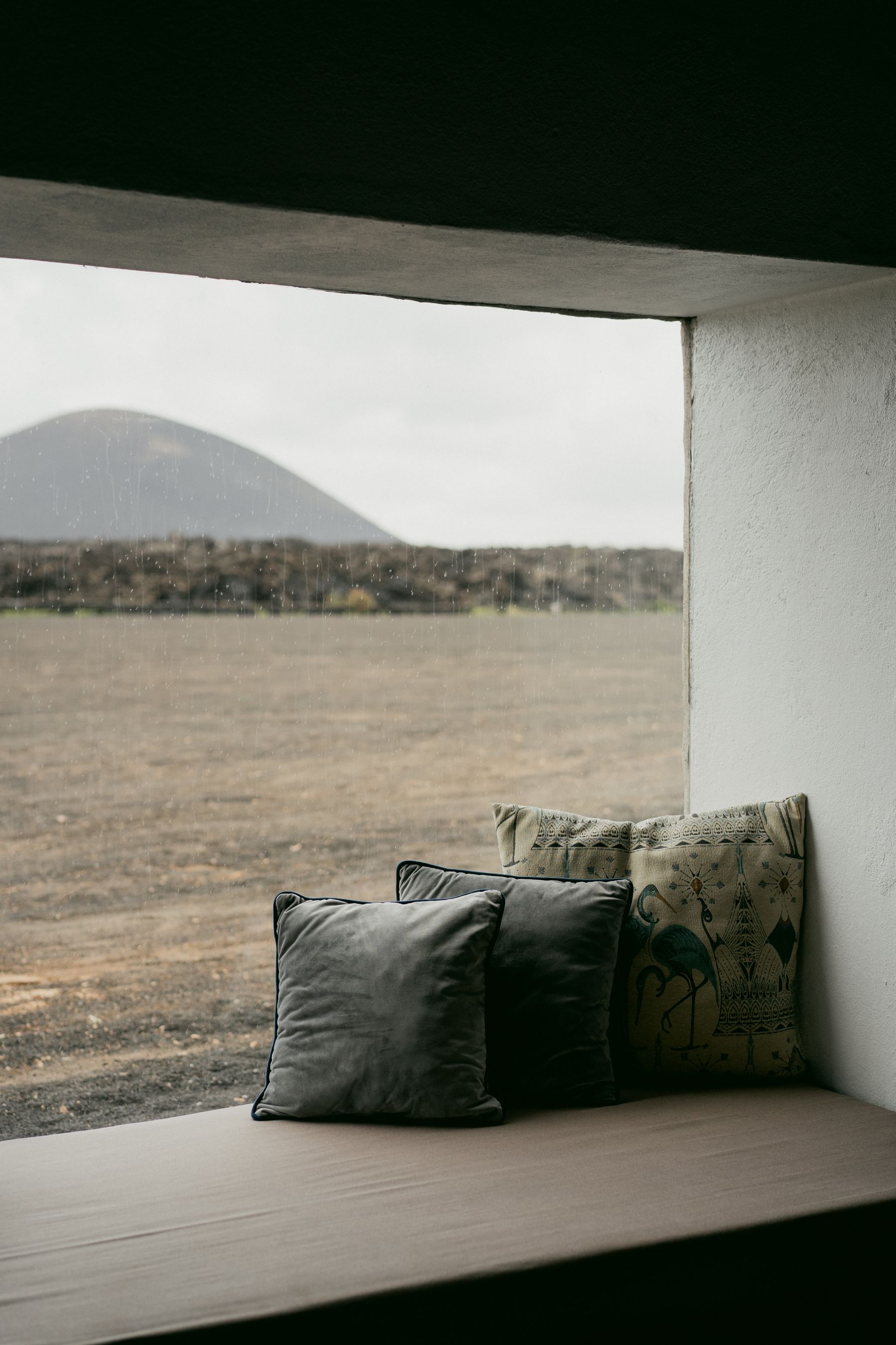 Layered grey and patterned pillows tucked into one end of a window niche