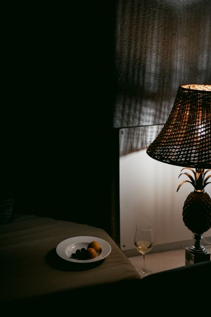 Warm, cozy interior with a wicker lamp, wine glass, and fruit plate.
