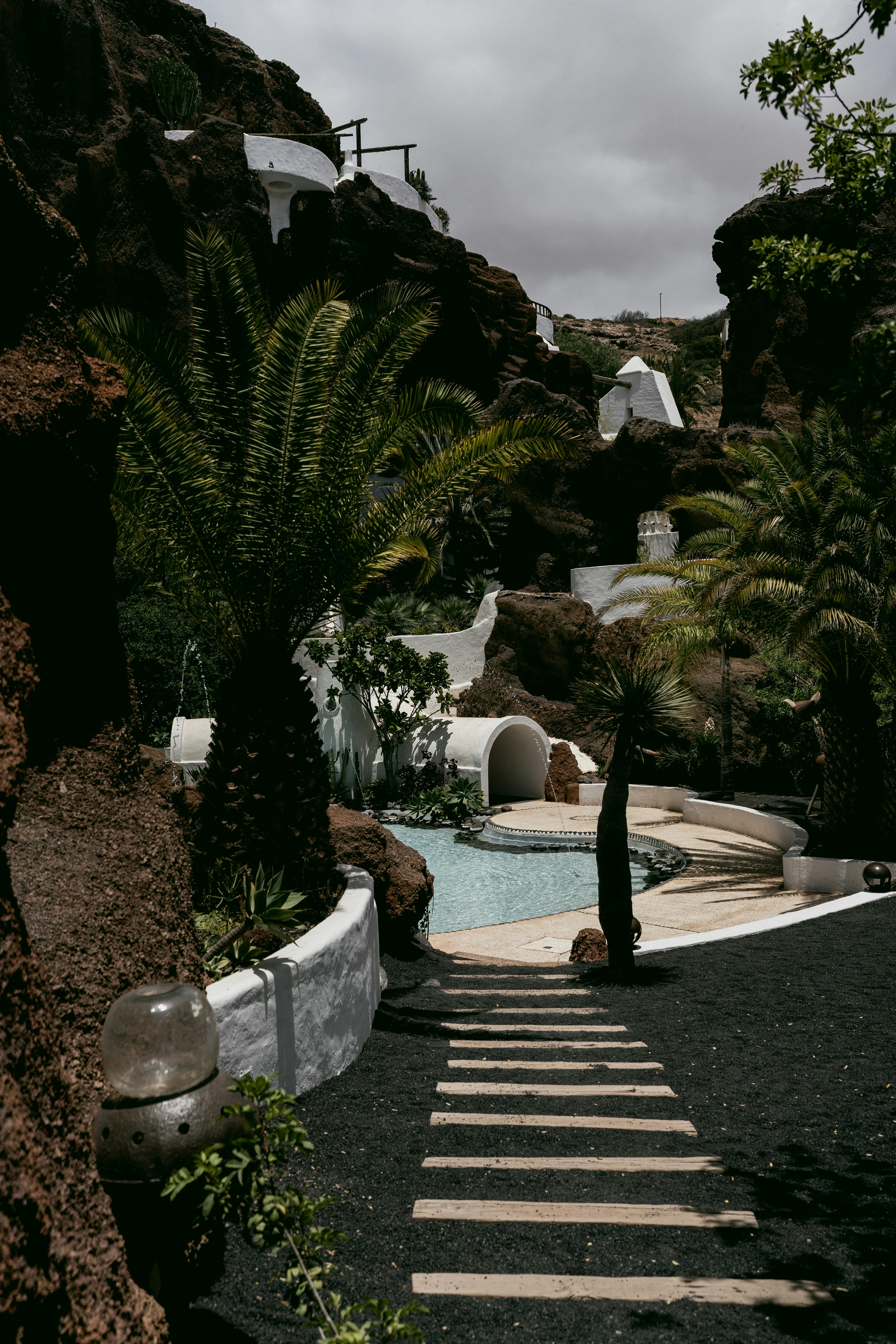 Tropical resort featuring palm trees, a pool, and unique architecture amidst rocky terrain.
