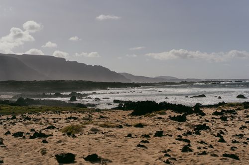 Free Serene rocky beach with waves crashing under clear sky. Stock Photo
