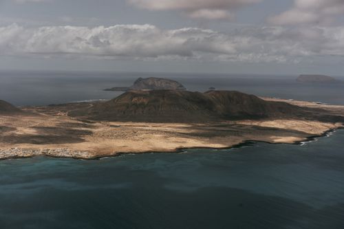 Free A stunning aerial view capturing the vast landscape of an island surrounded by the ocean under a cloudy sky. Stock Photo