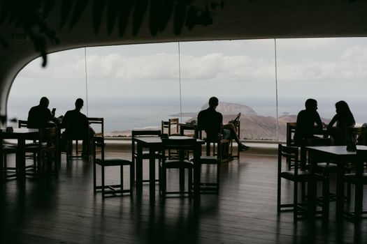 Silhouetted diners enjoy a serene ocean view from a stylish restaurant with large windows.
